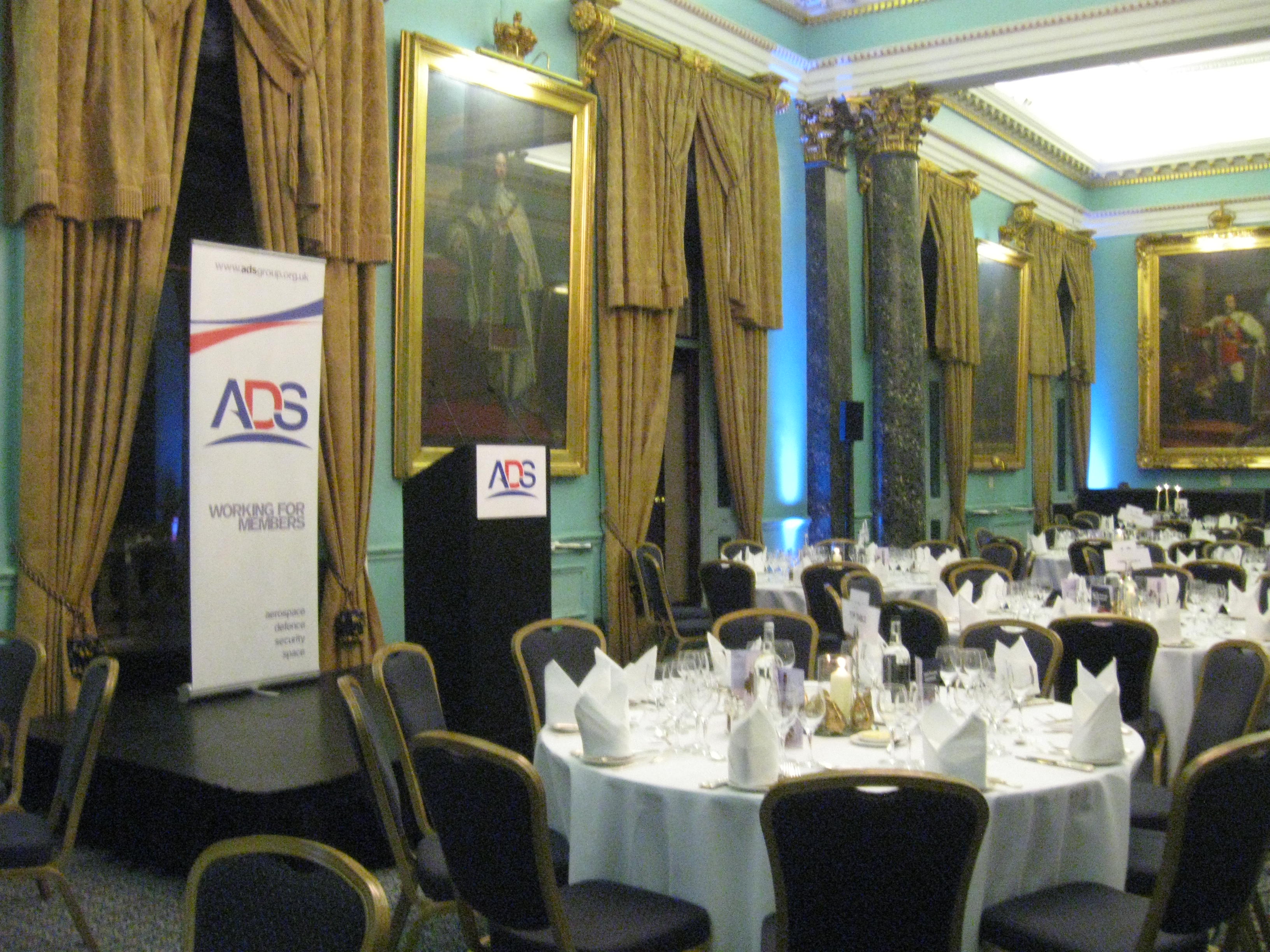 Tables laid in a grand room with gold curtains and an ADS sign