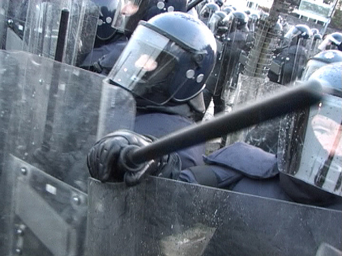 Close up shot of police dressed in riot gear, weilding batons and riot shields