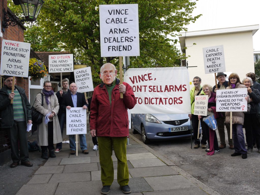 Protesters holding placards and a banner. The placard at the front reads 'Vince Cable - arms dealers' friend'