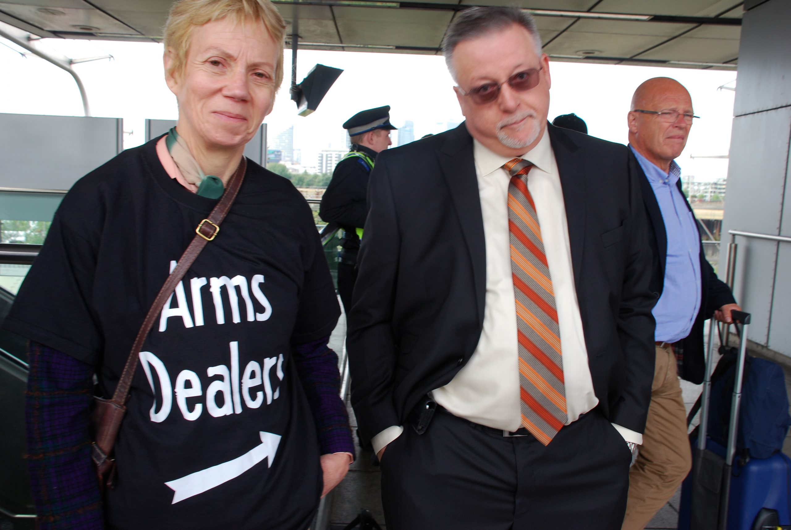 Activist with a T-shirt reading &quot;Arms Dealer&quot; and an arrow pointing sideways stands next to an arms fair delegate