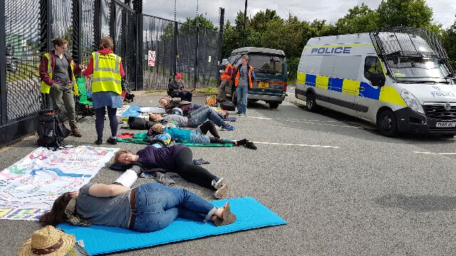 Five people lie in the road in front of a gate connected by arm tubes