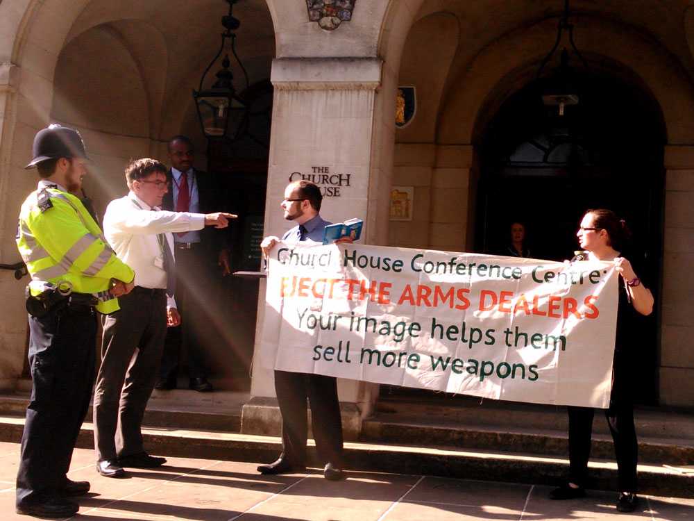 activists hold a banner up outside chruch house denouncing the conference