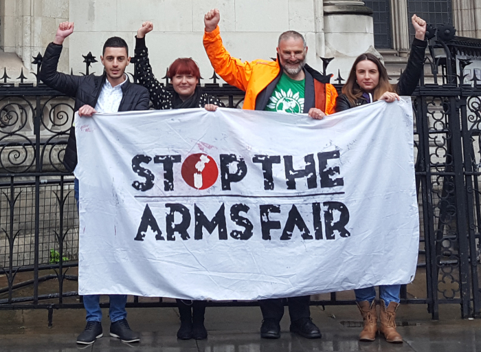 activists raise their fists behind a stop the arms fair banner