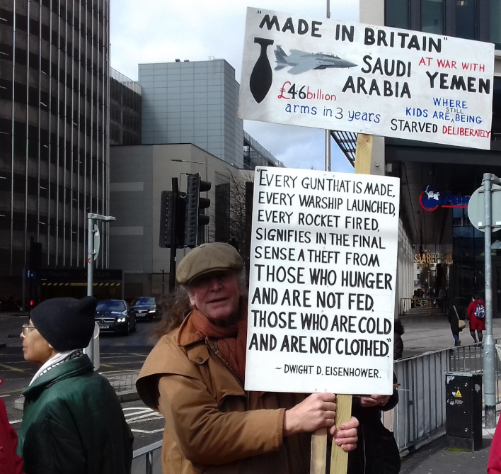 A protester on a pavement holding two placards.