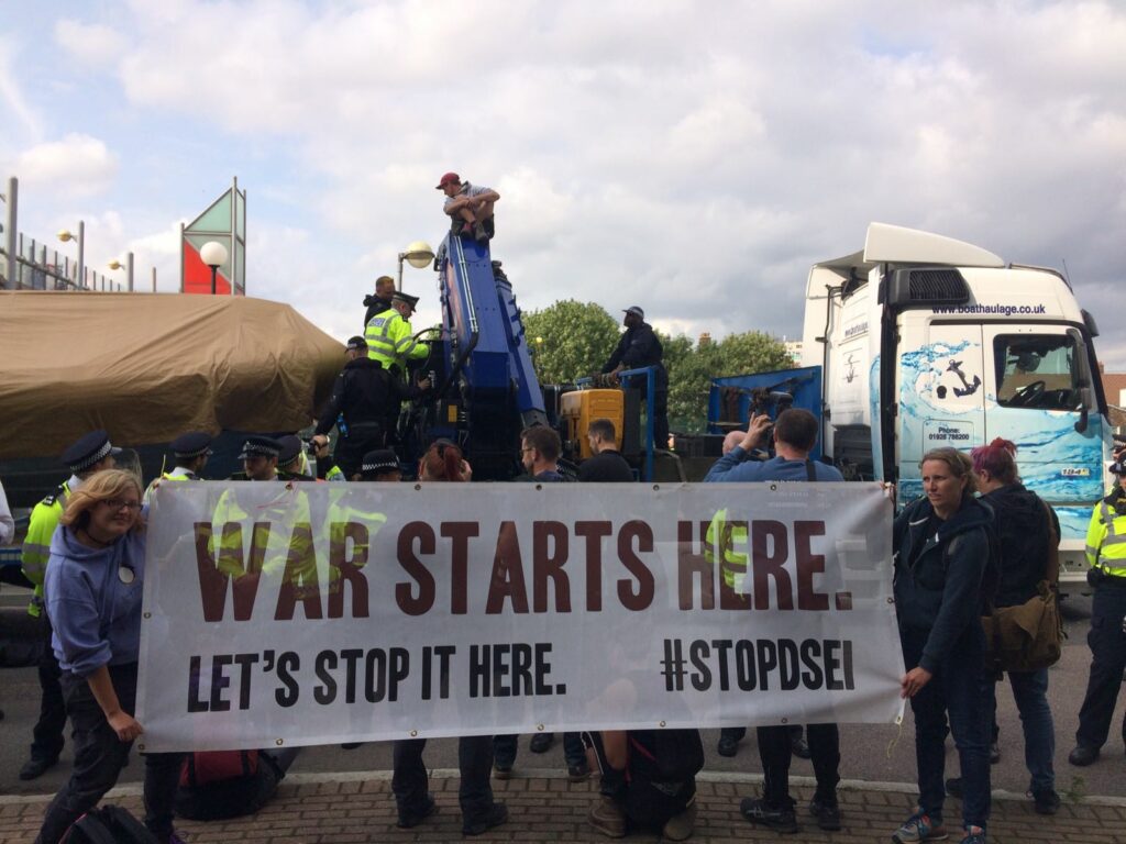 Activists at DSEI with banner saying 'war starts here.'
