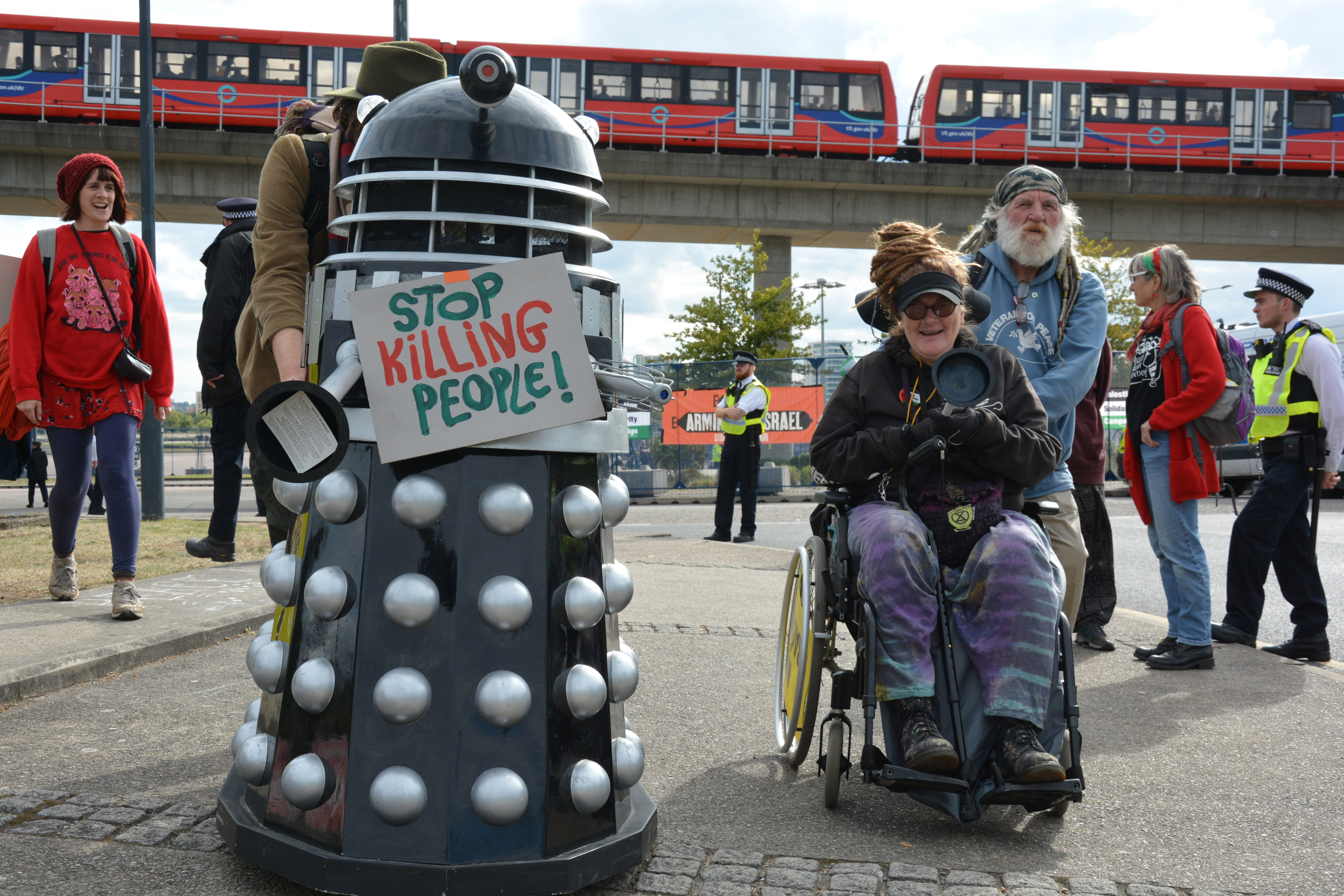 Dalek with banner saying 'stop killing people' outside DSEI