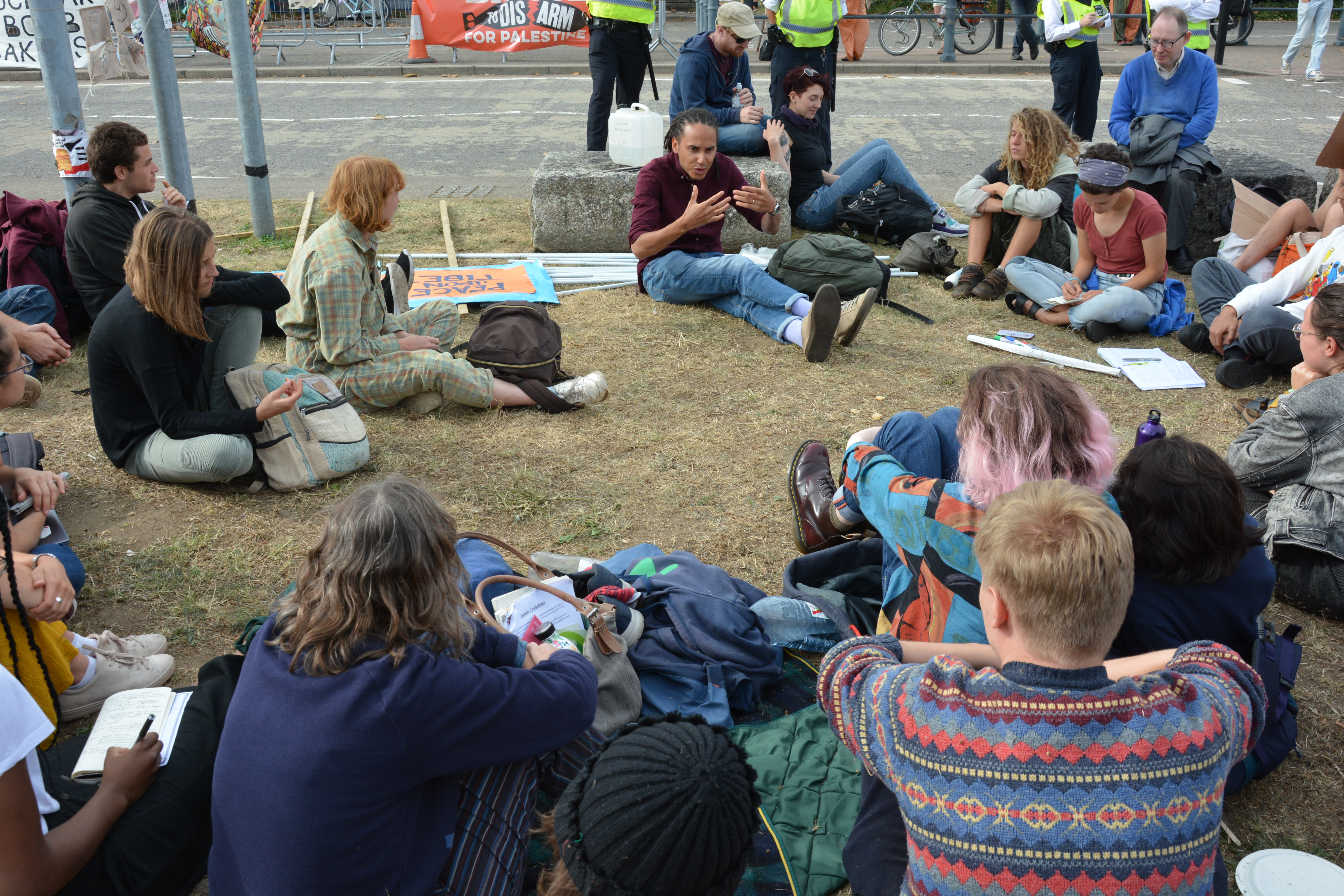 A group of people having discussions sitting on the ground next to a road.