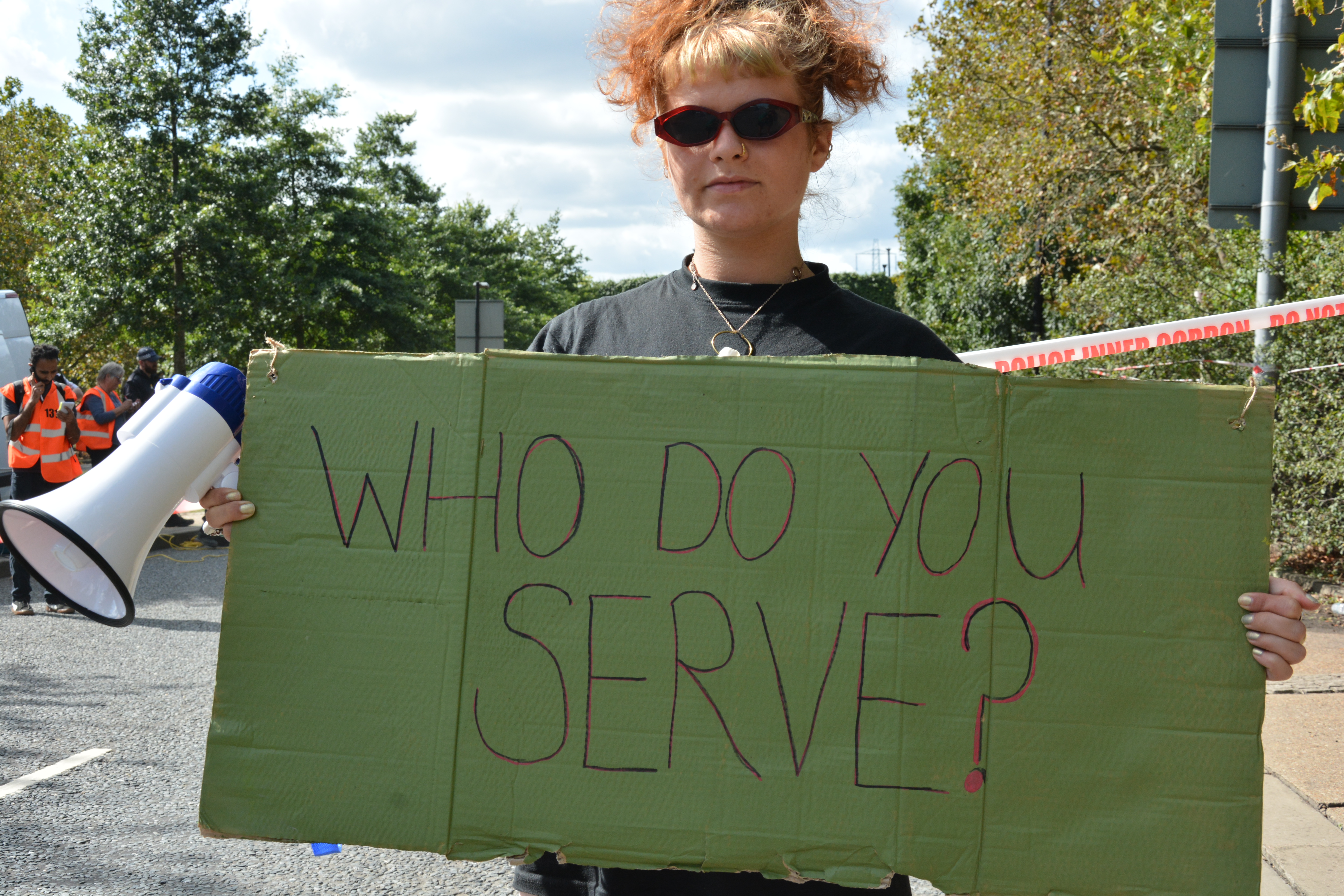 Activist outside DSEI with banner that reads 'who do you serve?'