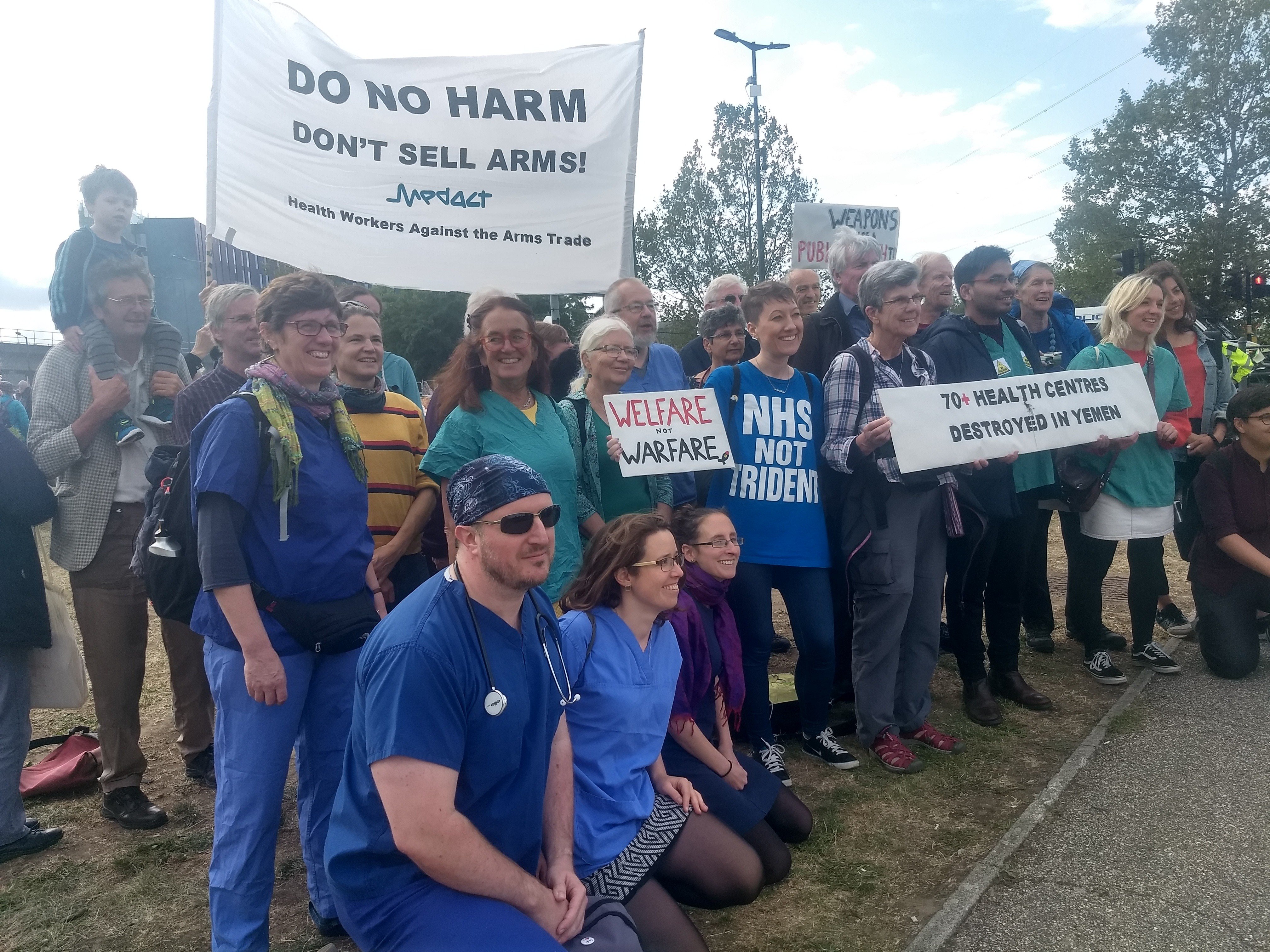 Medical professionals with banner saying 'do no harm, don't sell arms'