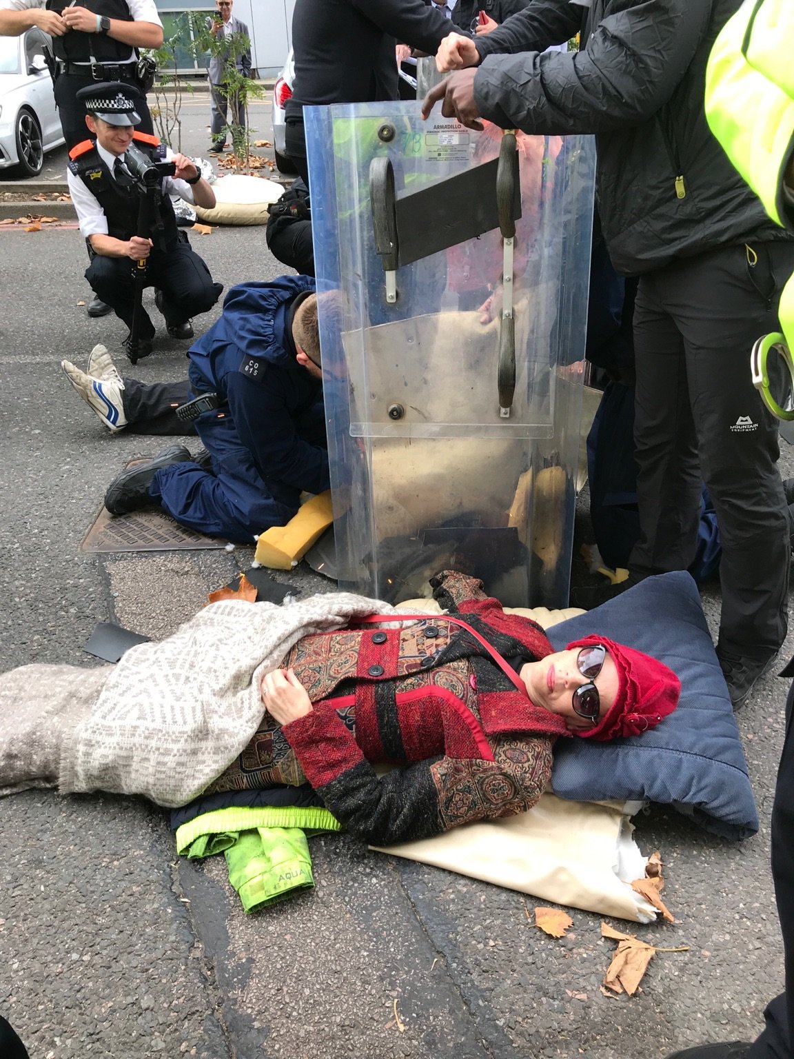 Protestors lying in a road with police around them. One police officer is videoing. Others appear to be removing lock-ons.