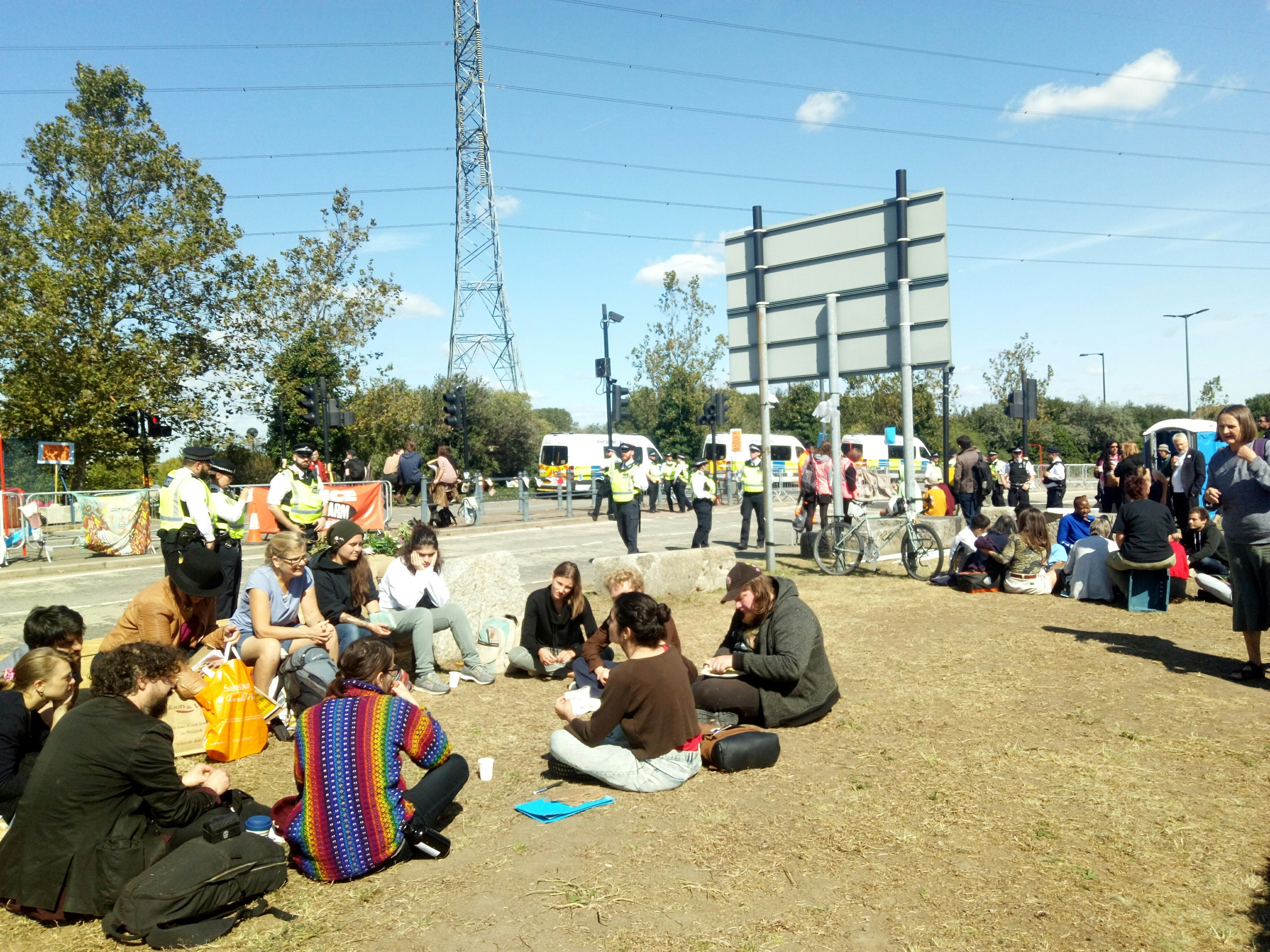Two groups of people sitting in circles on the ground having discussions. Police are nearby.