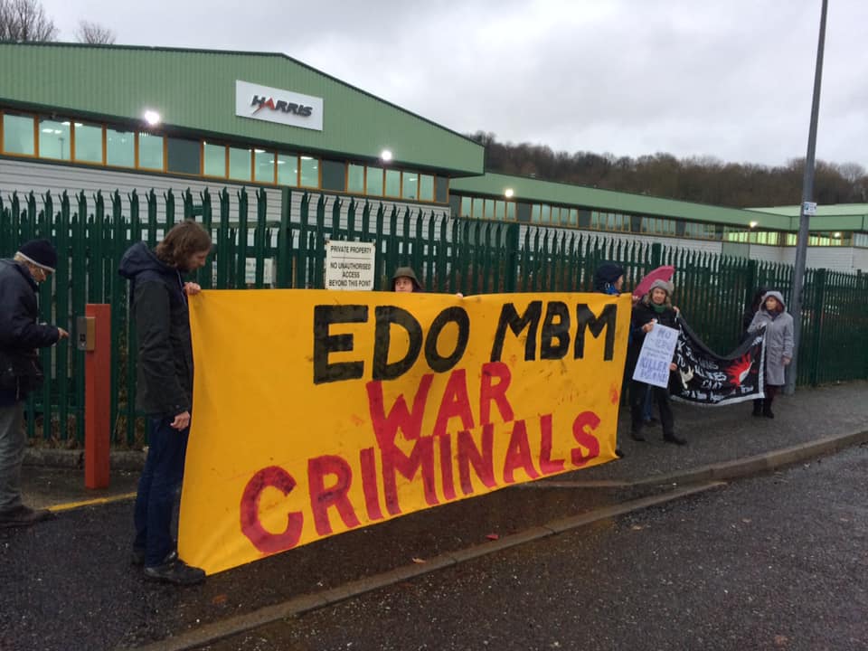 Activists hold a banner reading &quot;EDO war criminals&quot; outside the factory