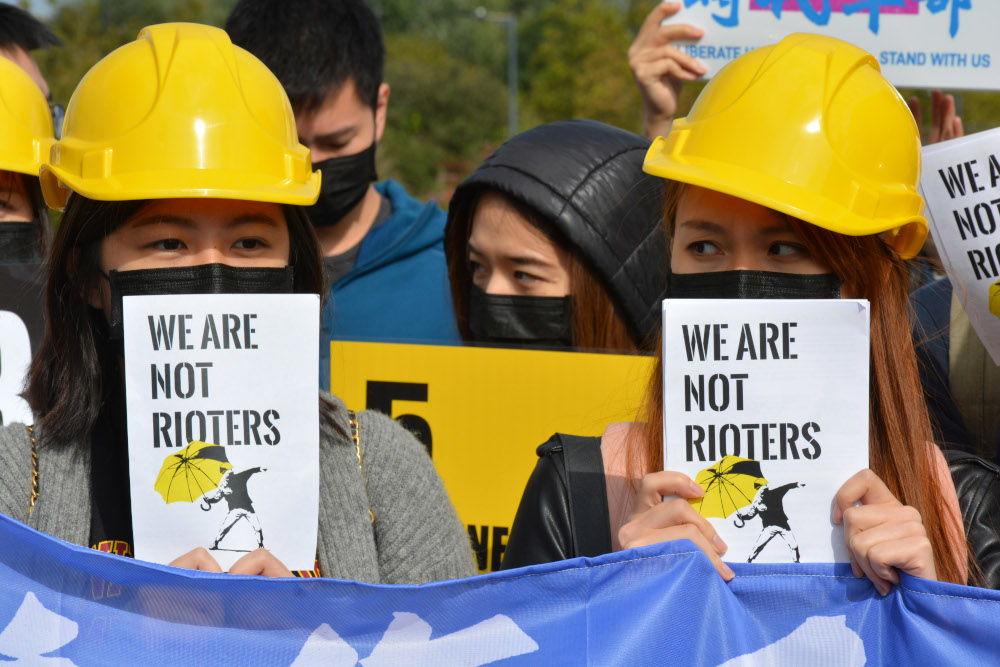 Protesters wearing yellow work helmets carrying signs saying "We are not rioters"