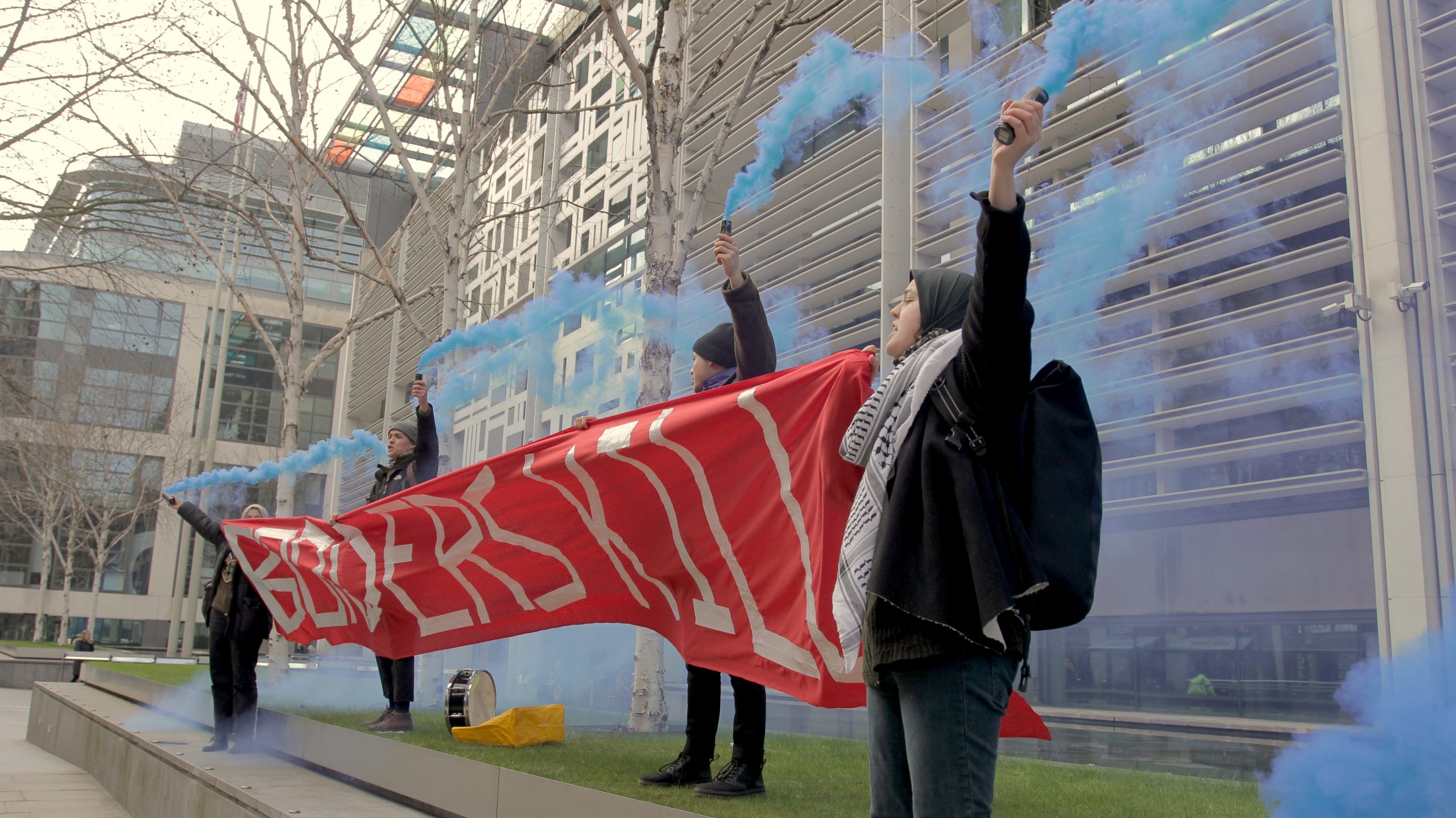Protestors hold a big red banner that states 'Borders Kill' and blue flares outside the Home Office