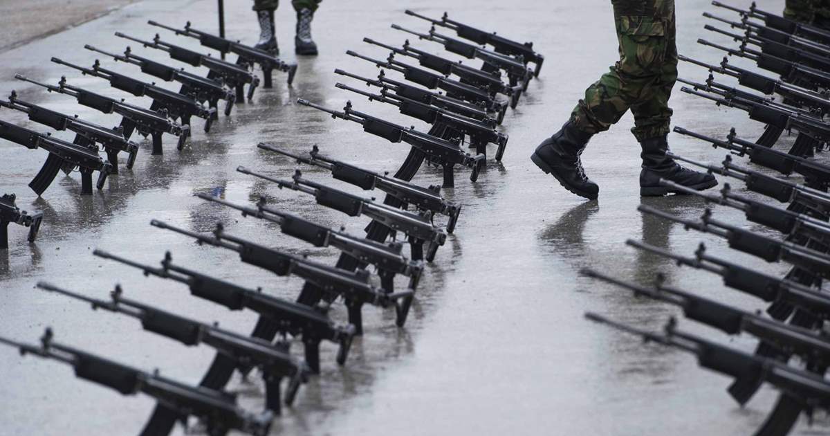 Automatic rifles with collapsible stocks lined up in a factory with a worker moving between them