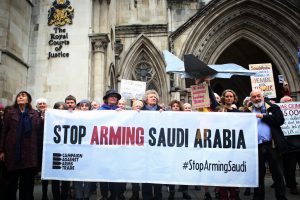 Supporters stand outside the Royal Courts of Justice, behind a banner saying Stop Arming Saudi Arabia, holding handmade placards with statistics about the war in Yemen