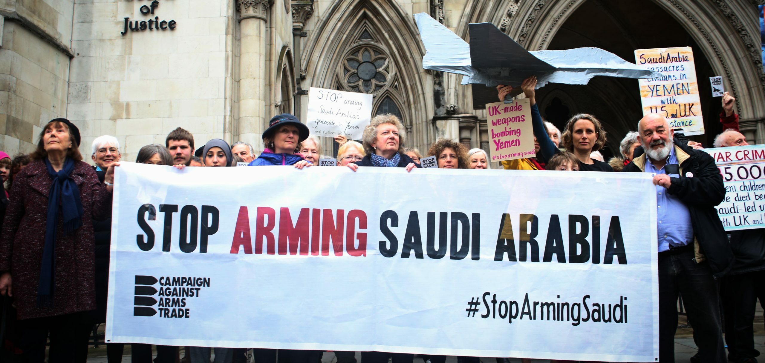 Supporters stand outside the Royal Courts of Justice, behind a banner saying Stop Arming Saudi Arabia, holding handmade placards with statistics about the war in Yemen