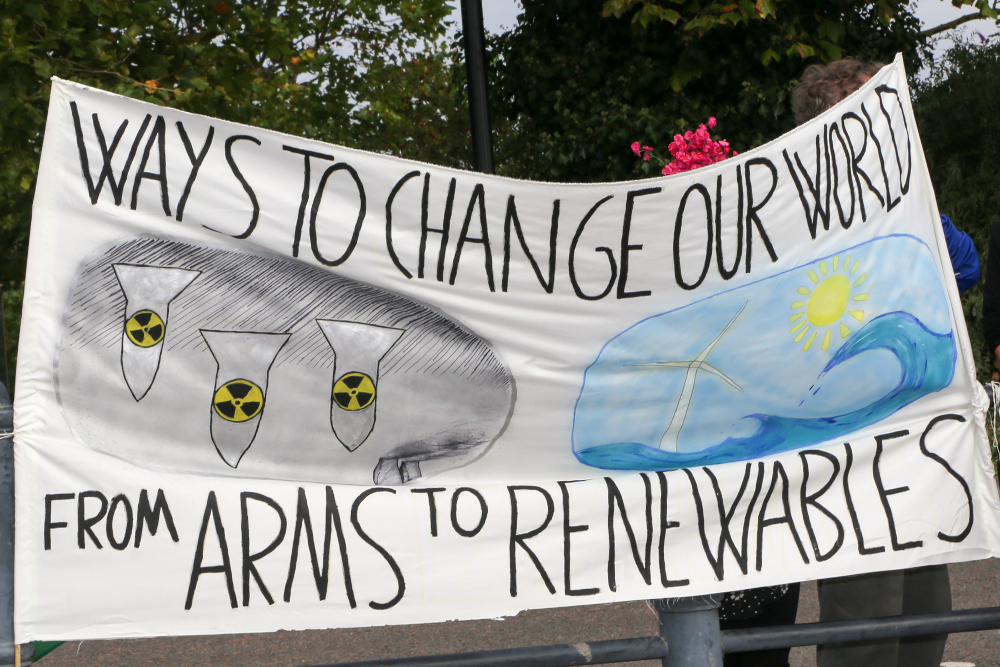 Ways to Change our world from arms to renewables banner, with drawings of falling nuclear bombs and picture of windmill and waves.