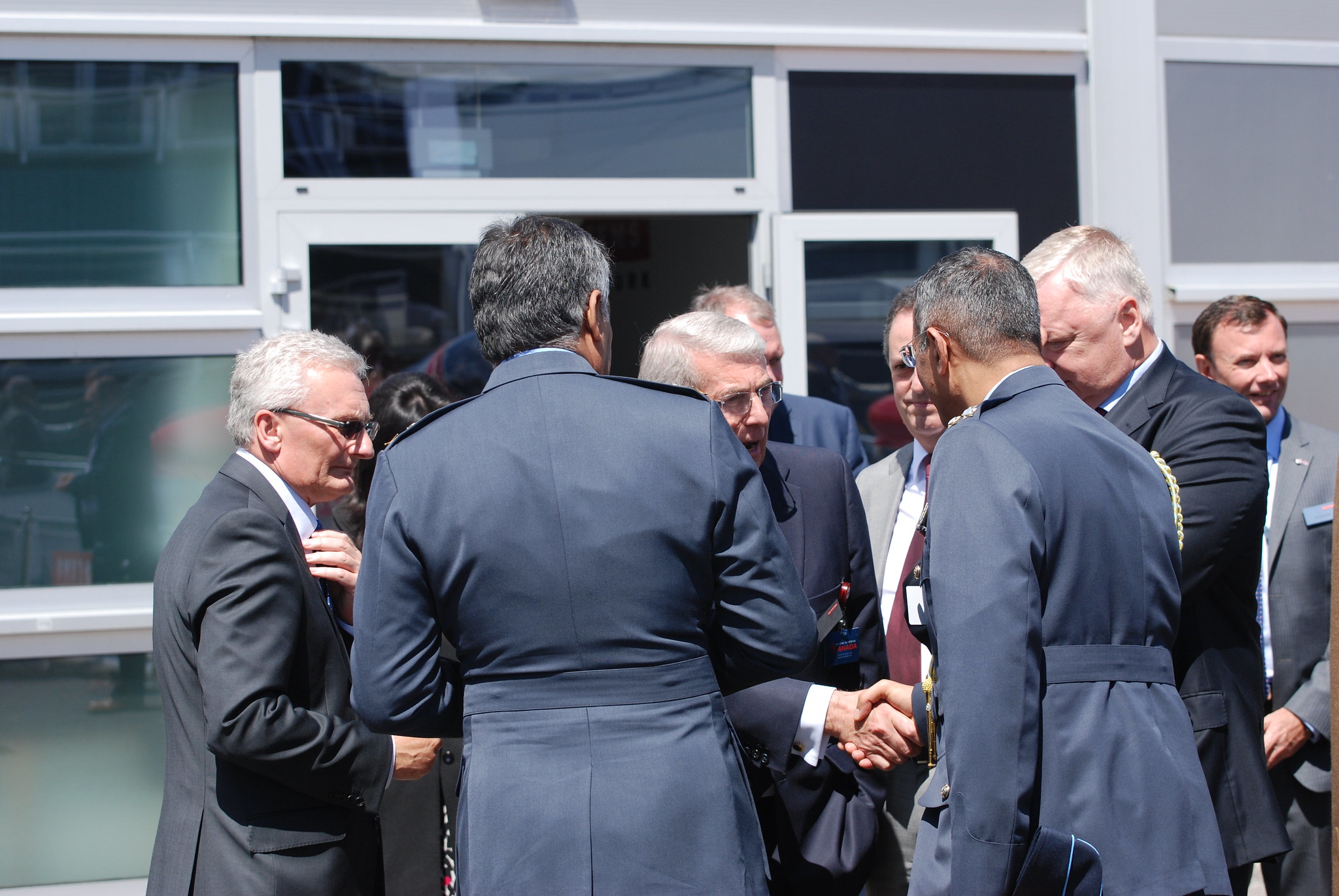 Seven men in suits talking, all with short greying hair