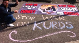 Kurdish activist next to banner and 'Stop War on Kurds' writing on pavement