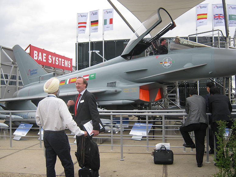 A Eurofighter Typhoon fighter jet being viewed by arms dealers with a BAE Systems logo in the background