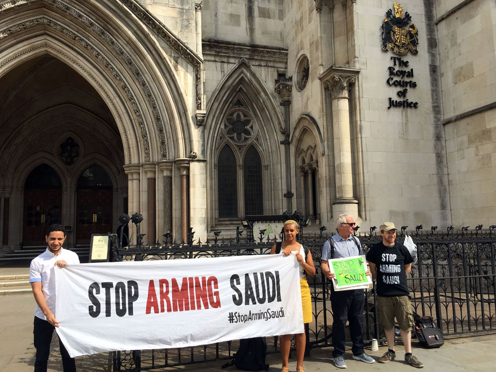 Campaigners with a Stop Arming Saudi banner outside Picture of the Royal Courts of Justice, including a man wearing a Stop Arming Saudi t-shirt printed white on black, and a person holding a green sign with the same message