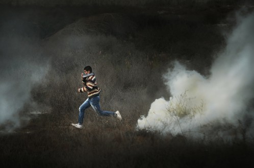 A young person runs across a bluured background in front of clouds of smoke