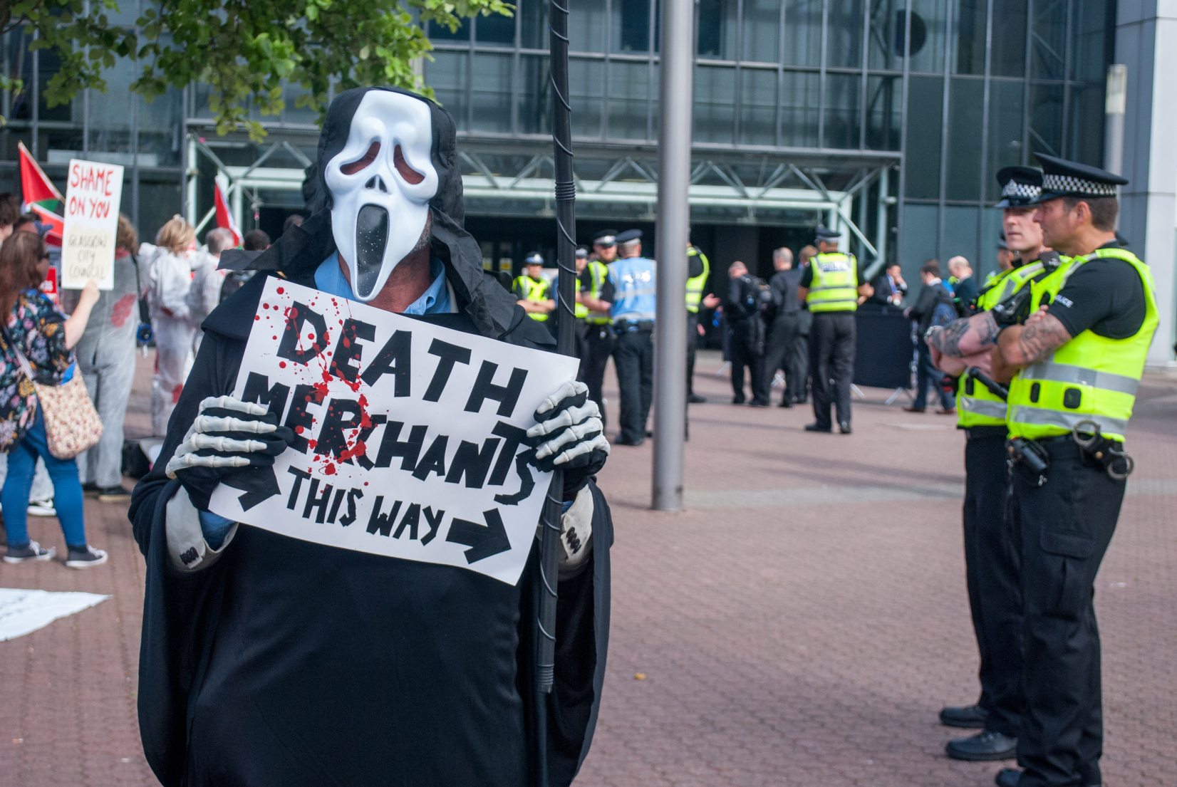 grim reaper next to police with sign 'death merchants this way'
