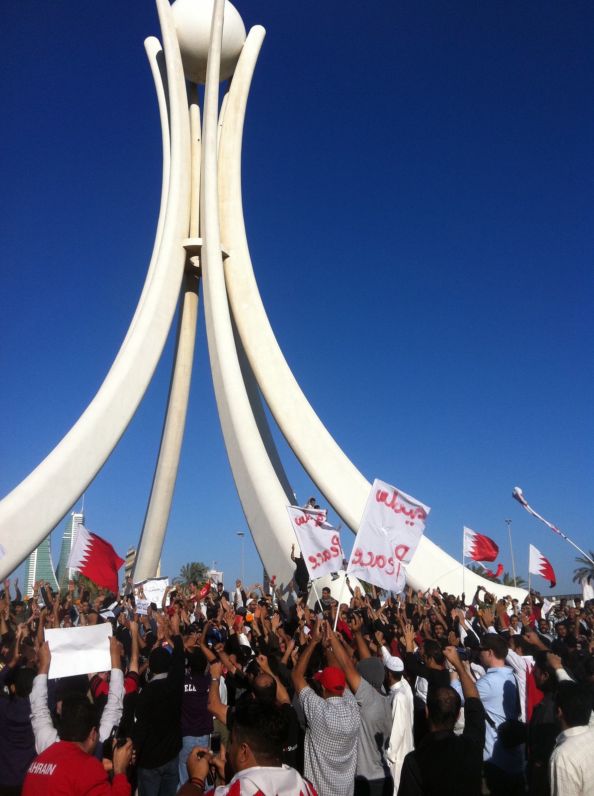 Protesters hold flags and banners in front on the Pearl Monument, a large white structure representing dhow &quot;sails&quot; projecting up to the sky, holding a pearl at the top