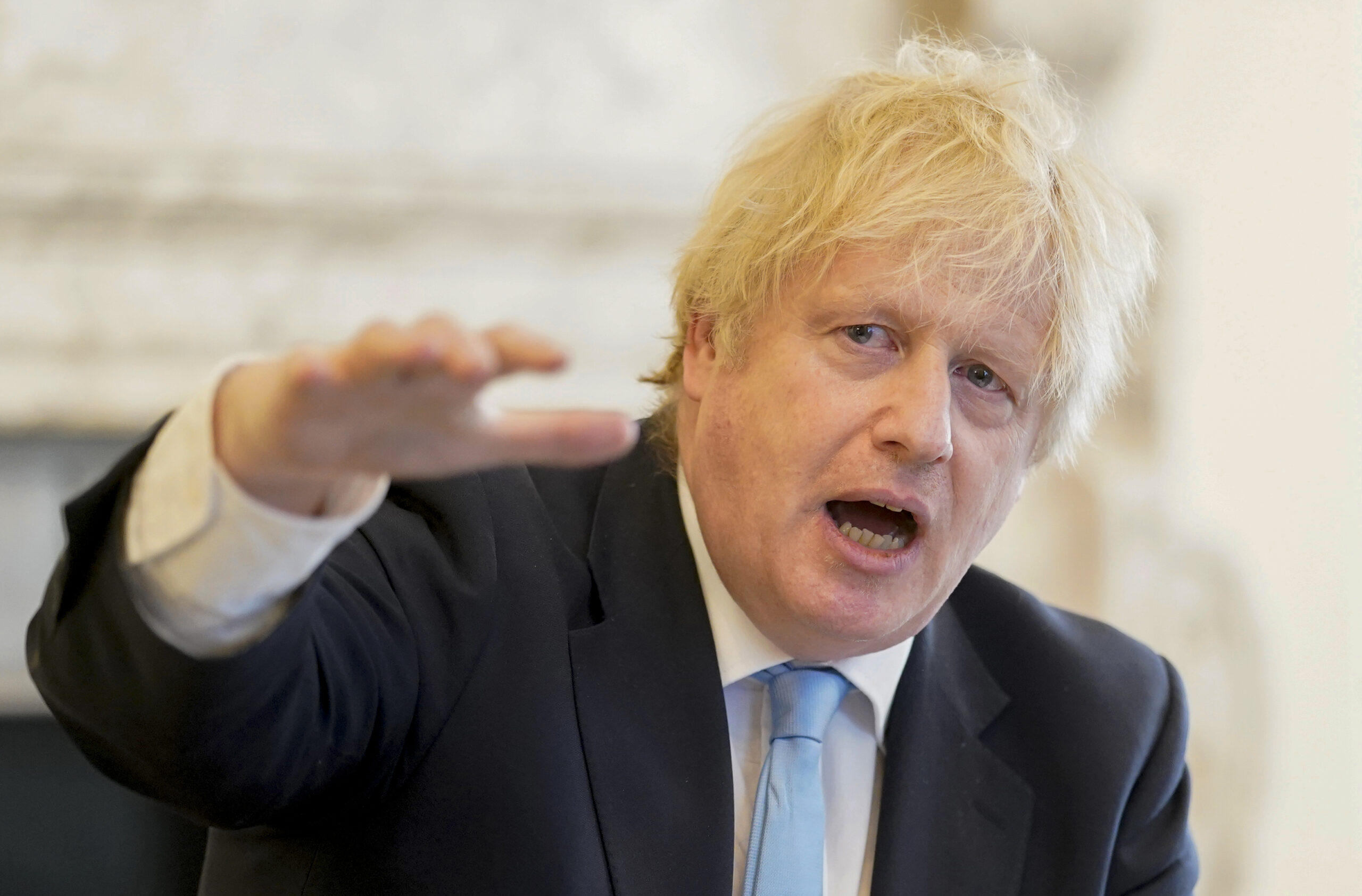 Prime Minister Boris Johnson, mid-speech looking past his slightly raised right hand, wearing a suit with blue tie