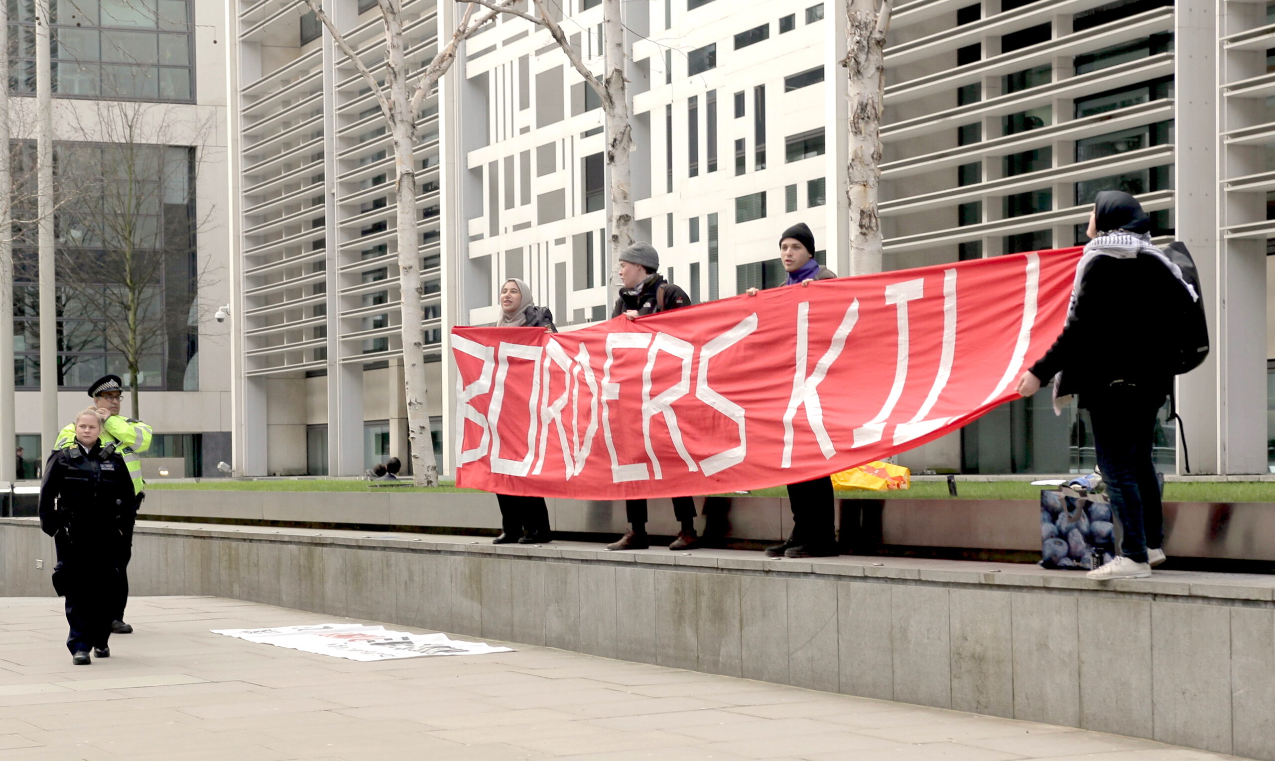 Four people holding a red banner that reads 'Borders Kill'