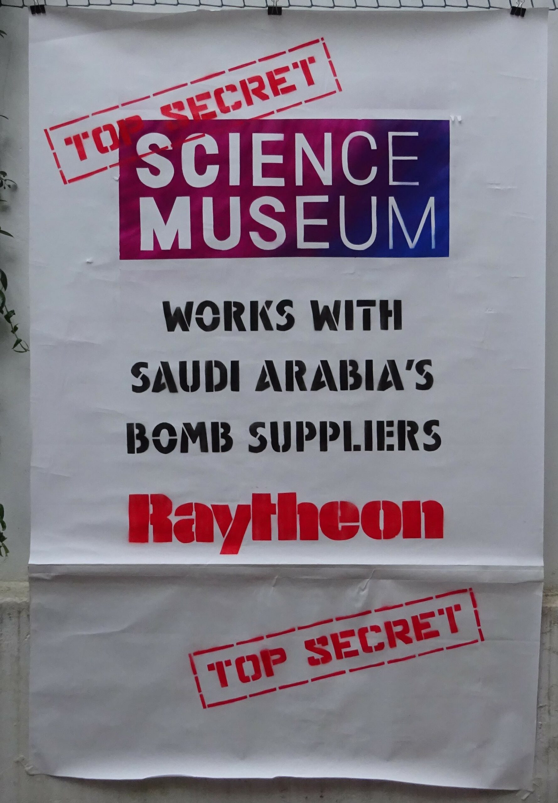A poster that reads 'Science Museum' 'Works with Saudi Arabia's Bomb Suppliers Raytheon' and has 'Top Secret' stamps.