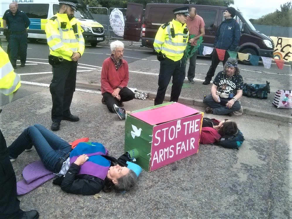 Protesters from the Ziegler case locked on in the middle of the road with a pink box reading &quot;Stop the Arms Fair&quot;