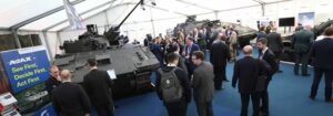 Arms dealers (men in suit and ties) at IAVS 2020 inspect Ajax vehicles (light tanks in camouflage patterns)