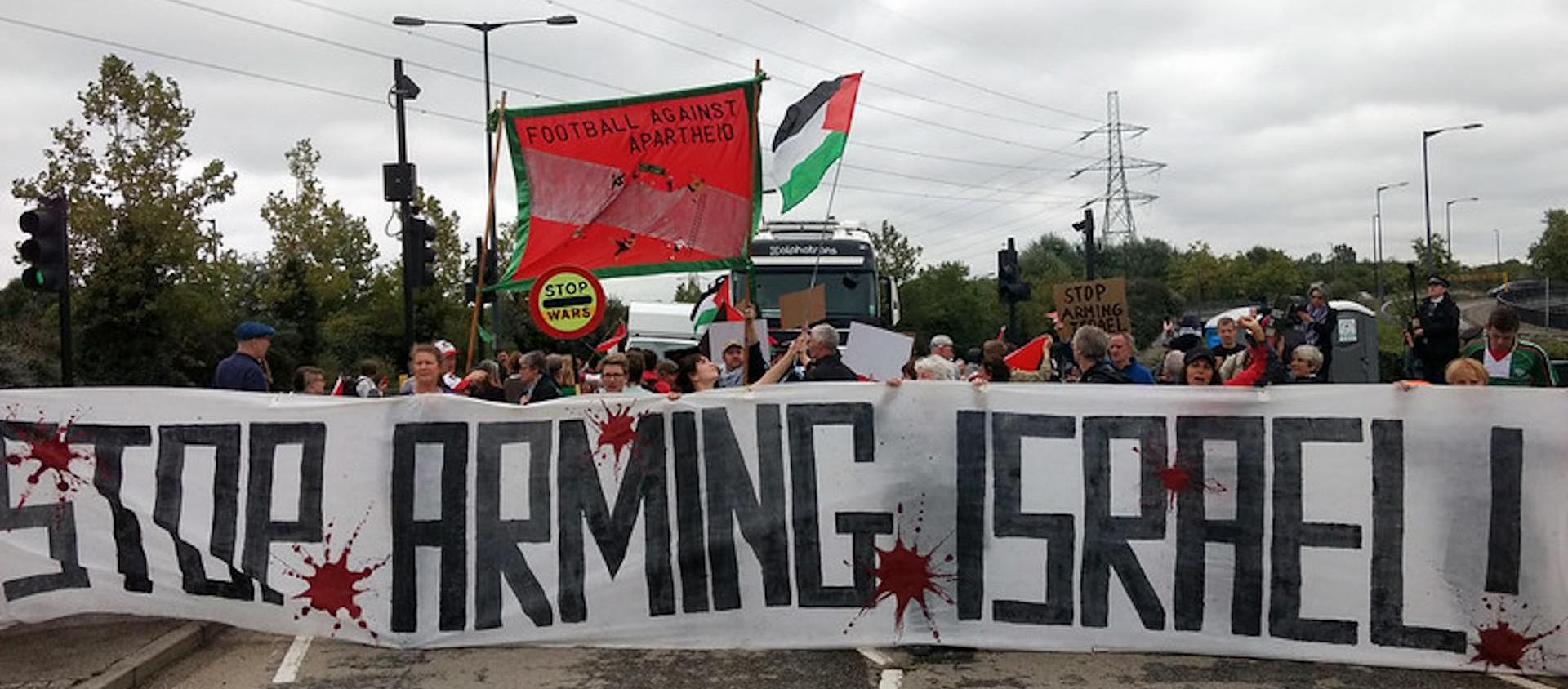 Protest blocking road to arms fair with a banner saying "Stop Arming Israel".