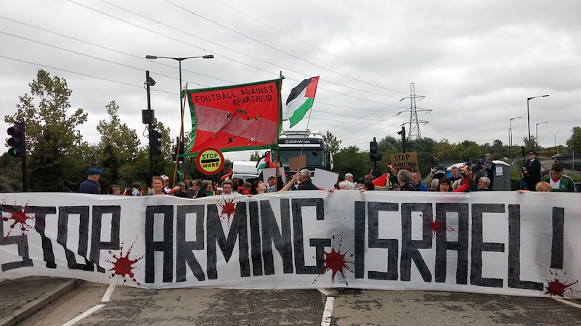 Banner stating &quot;Stop Arming Israel&quot; at a protest blocking the road to an arms fair