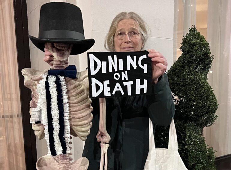 Protester at the ADS dinner in 2023 with a skeleton and a placard reading Dining in Death