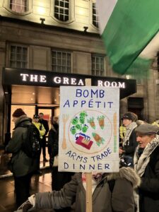 Protester with placard reading Bomb Appetit - arms trade dinner outside the ADS dinner