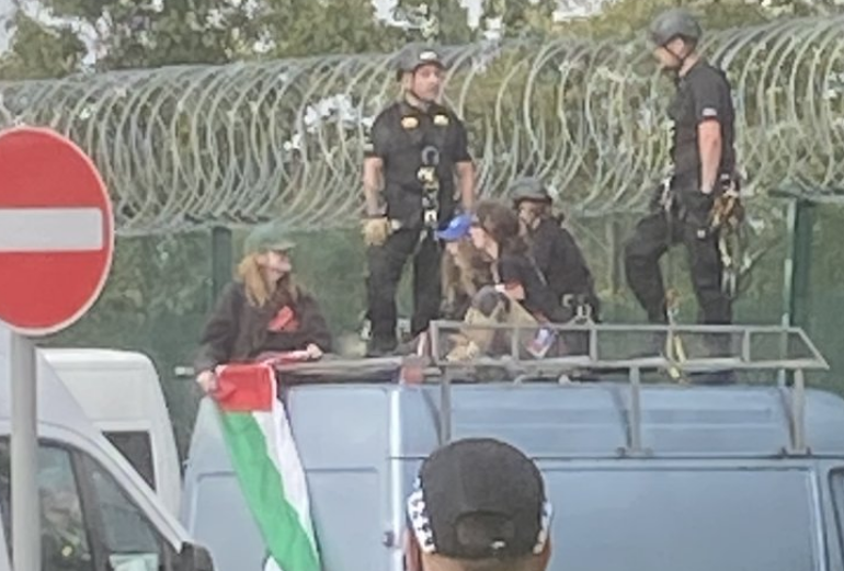 Image is of three people sittng on the roof of a van with police standing next to them outside Leonardo&#039;s Edinbrugh factory