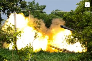 A forest with a fire blazing, the turrets of two artillery guns seen in the bushes and on the ground