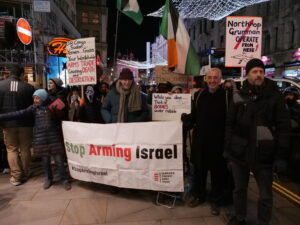 Protesters with placards stand behind a "Stop Arming Israel" banner.