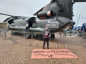 Campaigner in front of a Royal Air Force CH-47 Chinook helicopter marked up with text saying "Royal Air Force Regular and Reserve". In front of them is a banner saying "Break the Kill Chain"
