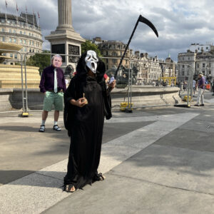 Death addresses the audience in Trafalgar Square while Keir Starmer looks on
